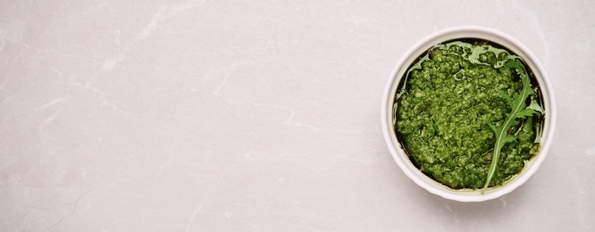 Bowl of tasty arugula pesto and space for text on light table, top view. Banner design