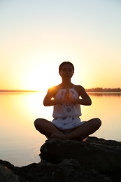 Photo of Woman practicing yoga near river on sunset. Healing concept