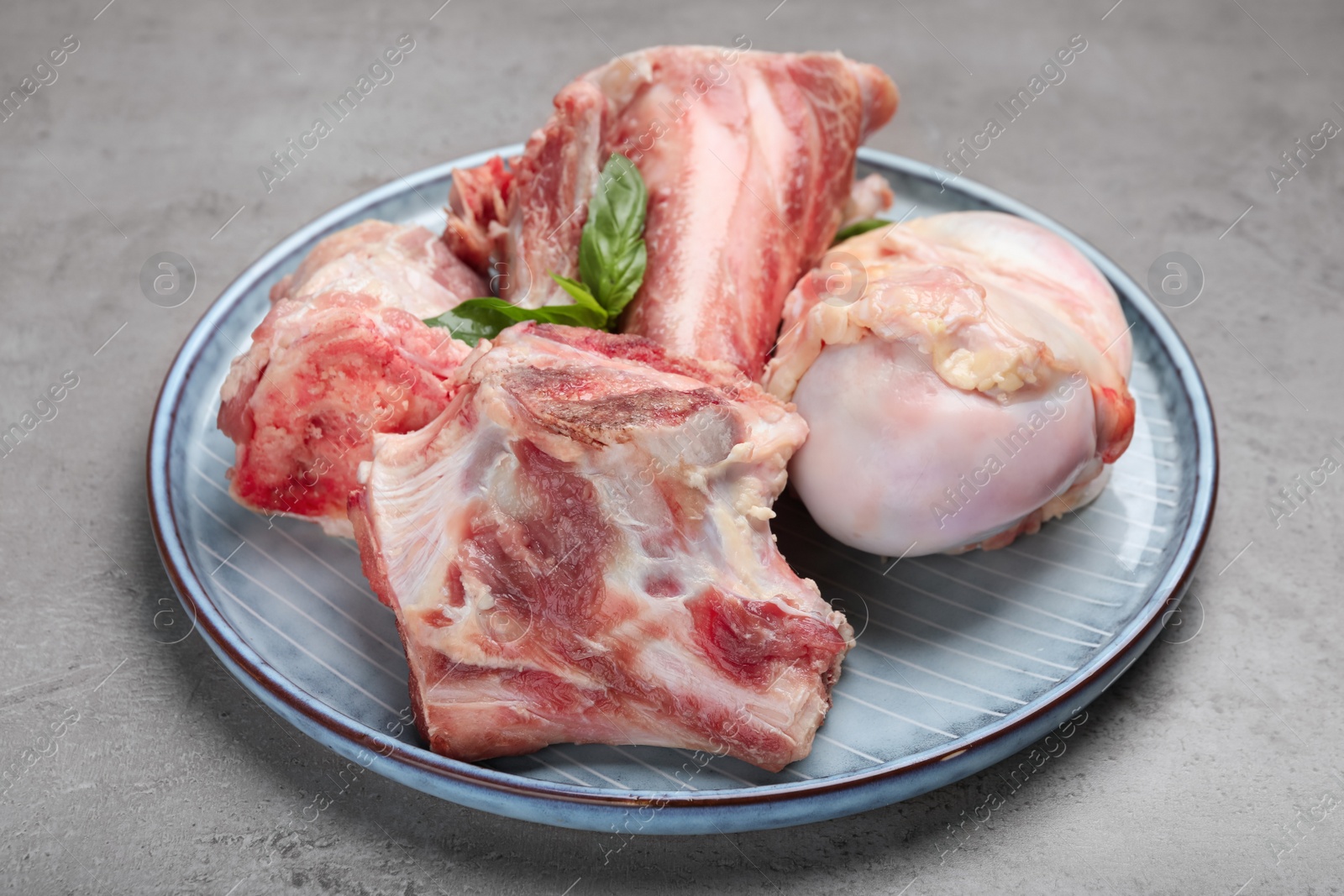 Photo of Plate with raw chopped meaty bones and basil on grey table