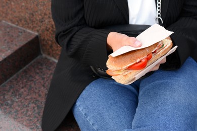 Woman holding tasty sandwich with vegetables outdoors, closeup. Street food