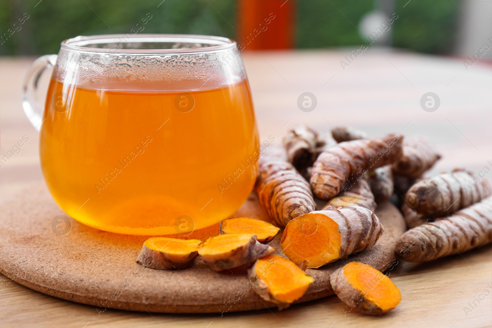 Photo of Glass cup of hot tea and fresh turmeric roots on wooden table, closeup