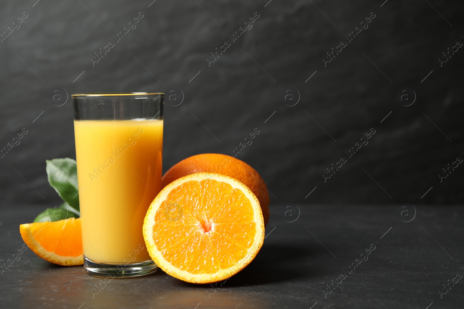 Photo of Glass of orange juice and fresh fruits on grey table. Space for text