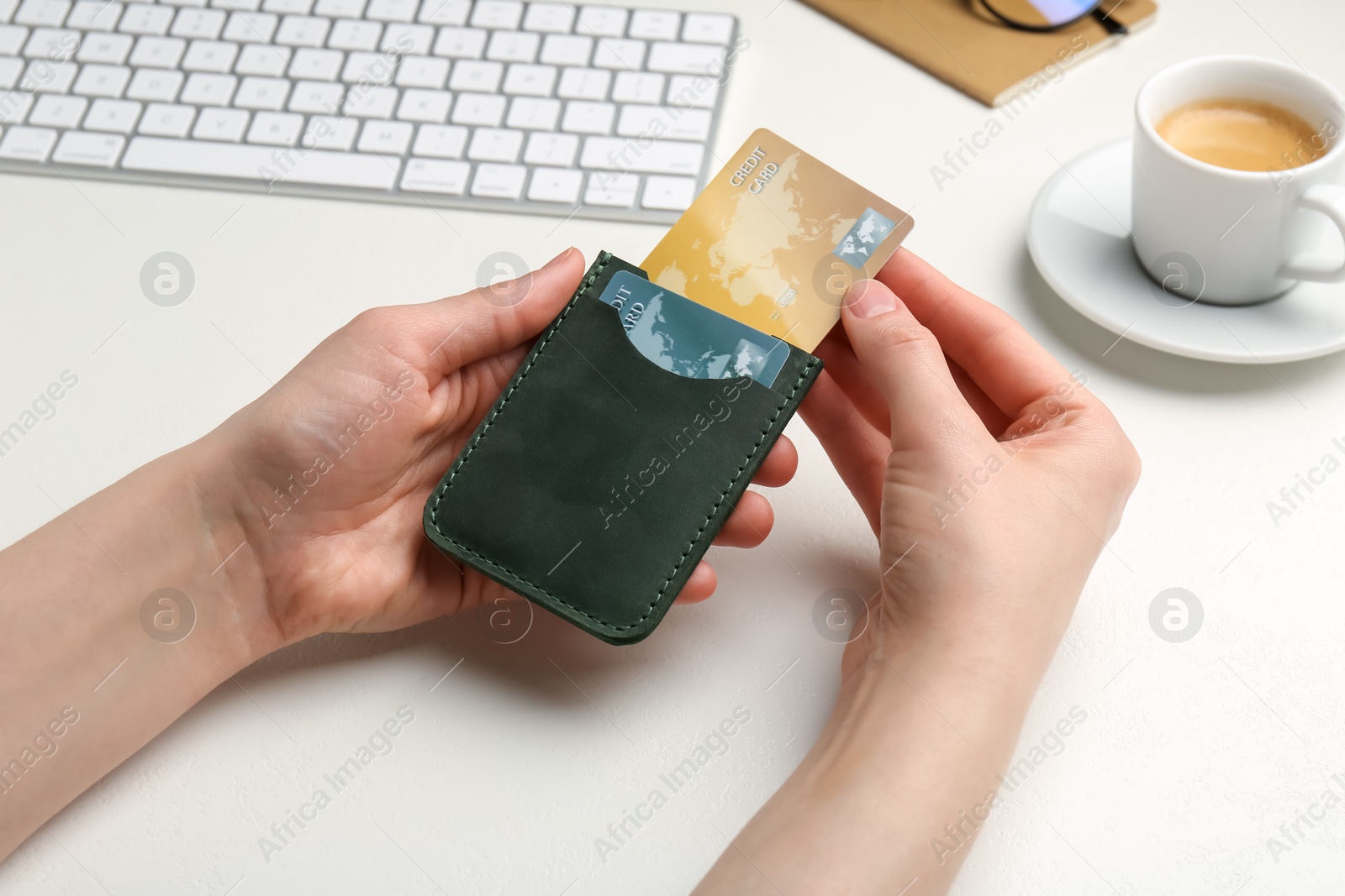 Photo of Woman holding leather card holder with credit cards at white table, closeup