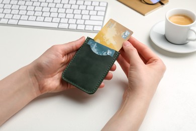 Woman holding leather card holder with credit cards at white table, closeup