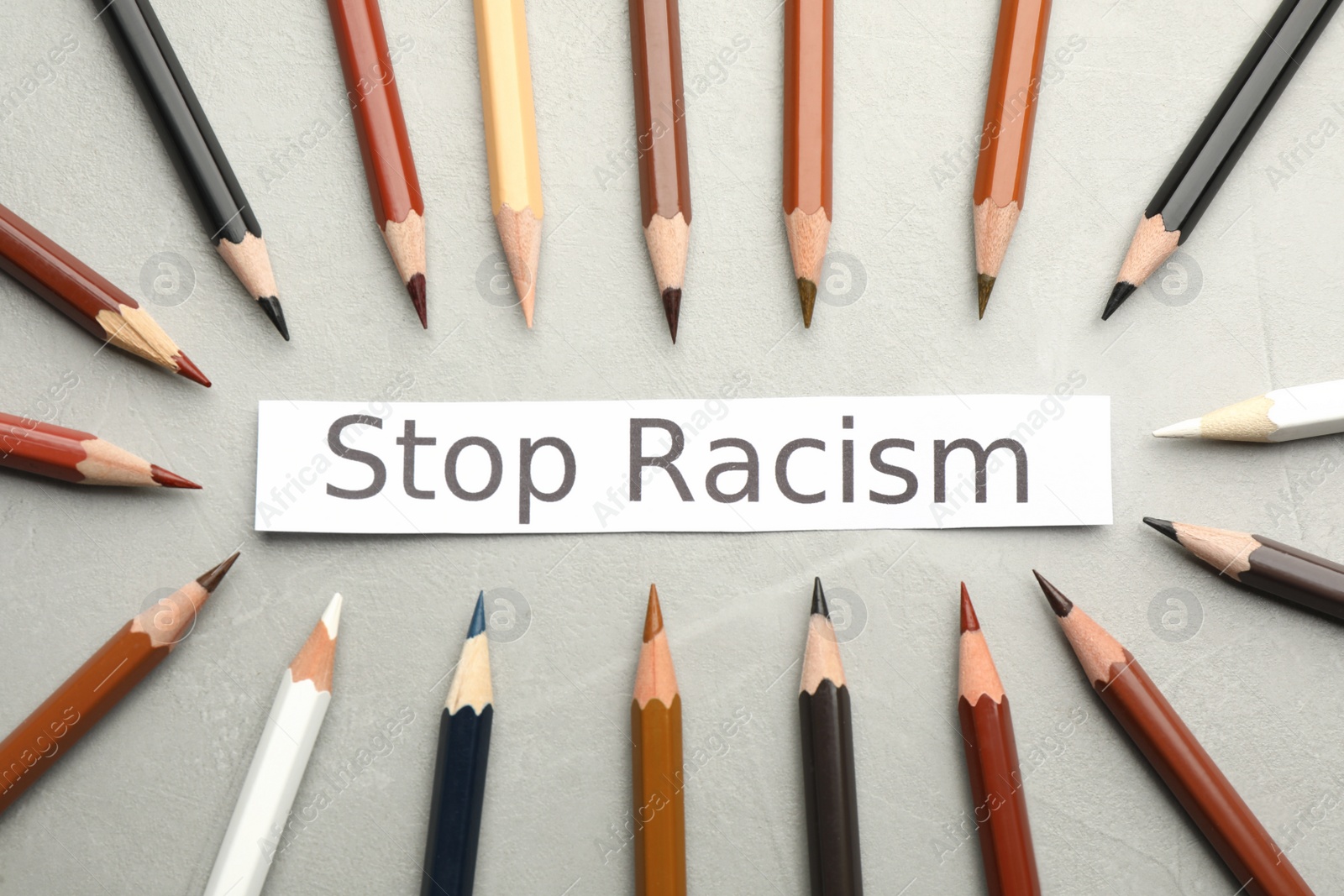 Photo of Phrase Stop Racism and colorful pencils on light grey table, flat lay