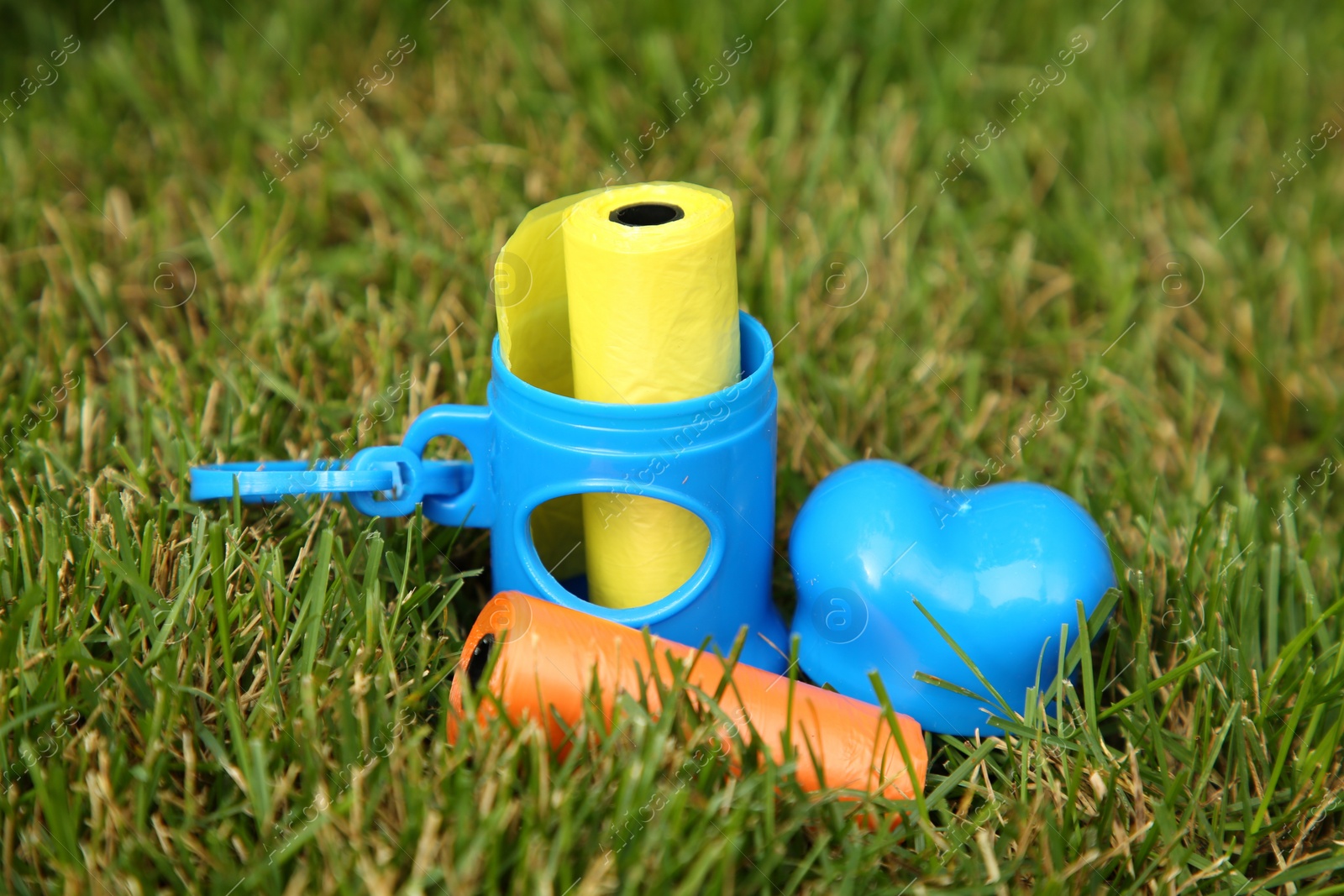 Photo of Rolls of colorful dog waste bags on green grass outdoors