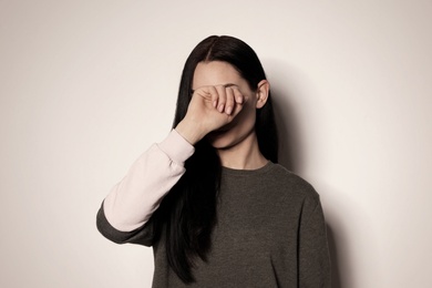 Photo of Young woman covering face against light background