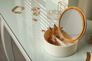 Photo of Jewelry box with mirror and stylish golden bijouterie on table, space for text