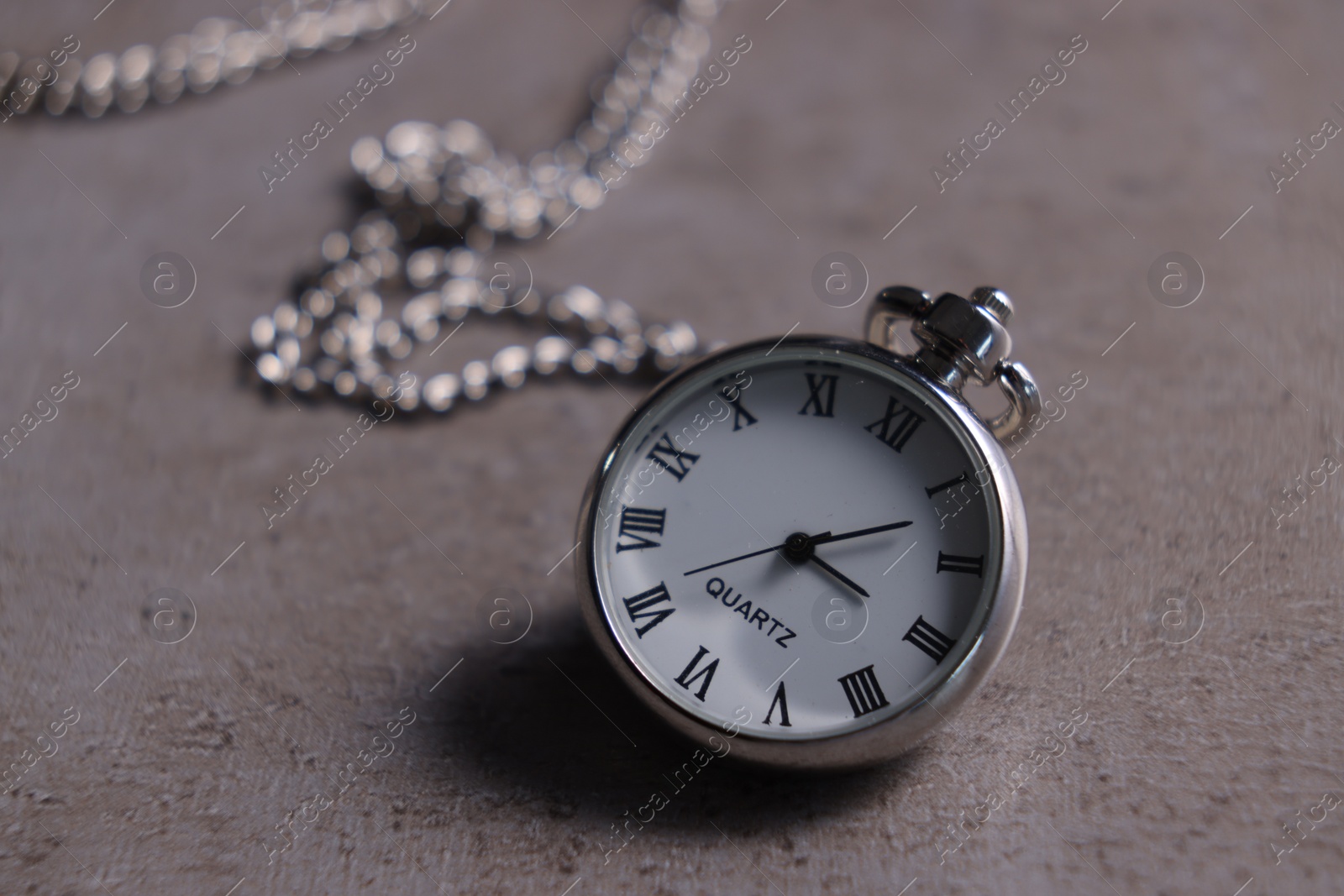 Photo of Silver pocket clock with chain on grey textured table, closeup