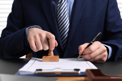 Photo of Notary with pen stamping document at table in office, closeup
