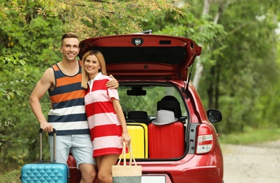 Happy couple near car trunk with suitcases outdoors