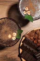 Dessert bowls of delicious hot chocolate with hazelnuts and fresh mint on wooden table, flat lay