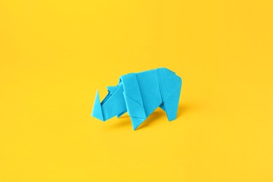 Origami art. Handmade light blue paper rhinoceros on yellow background