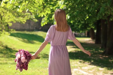 Photo of Woman with bouquet of spring flowers in park on sunny day, back view