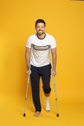 Photo of Man with injured leg using crutches on yellow background