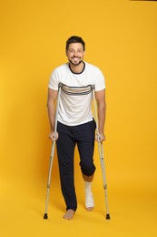 Man with injured leg using crutches on yellow background