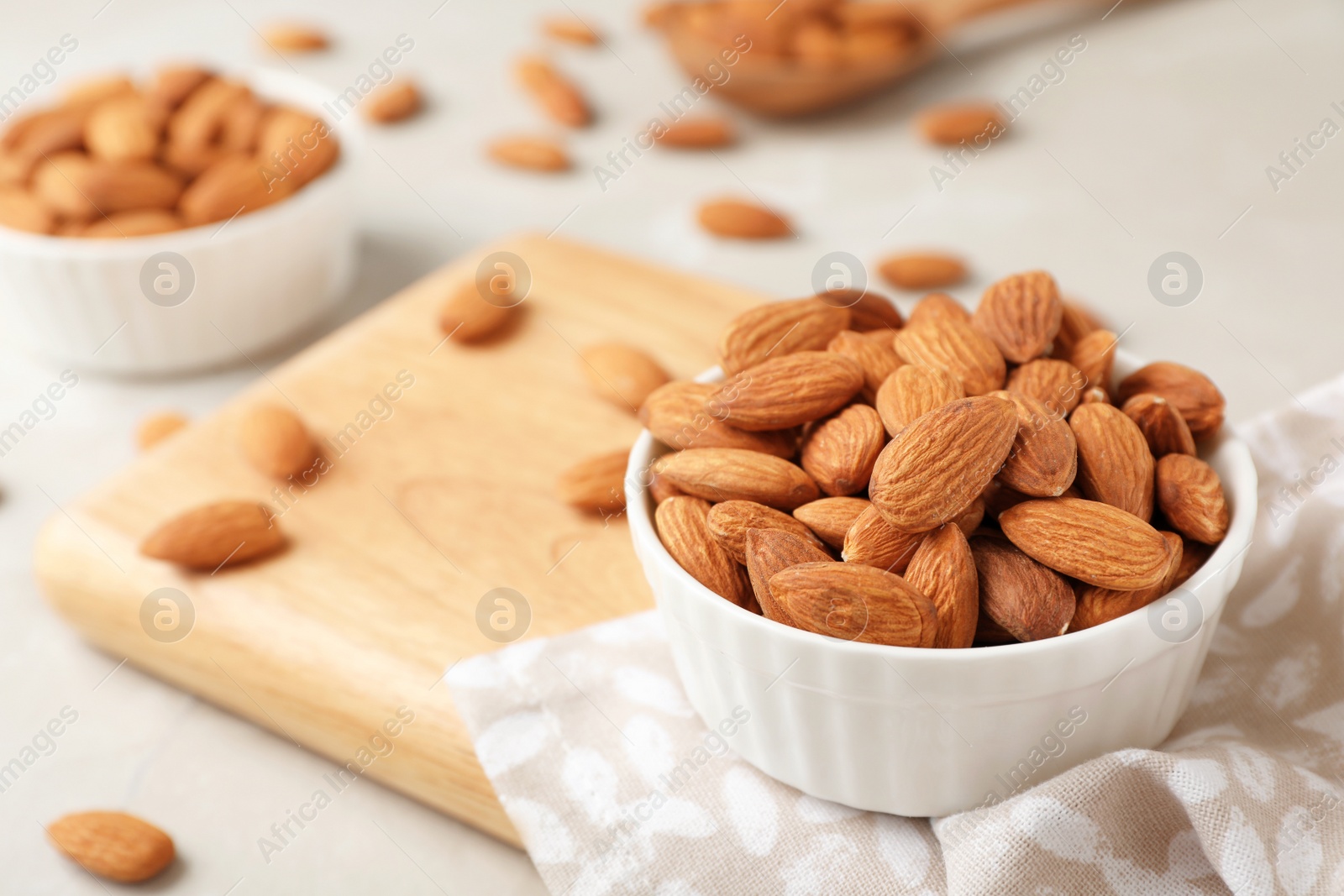 Photo of Wooden board with tasty organic almond nuts in bowl on table. Space for text