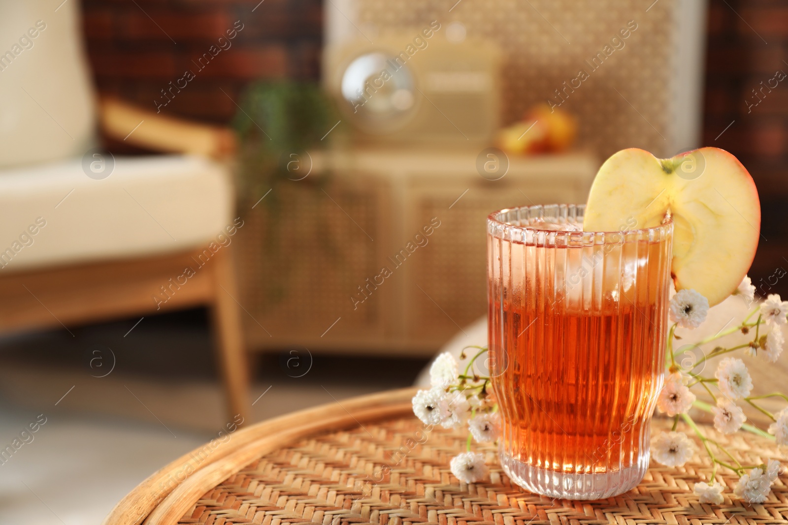 Photo of Glass of tasty cider and flowers on wicker table in room, space for text. Relax at home