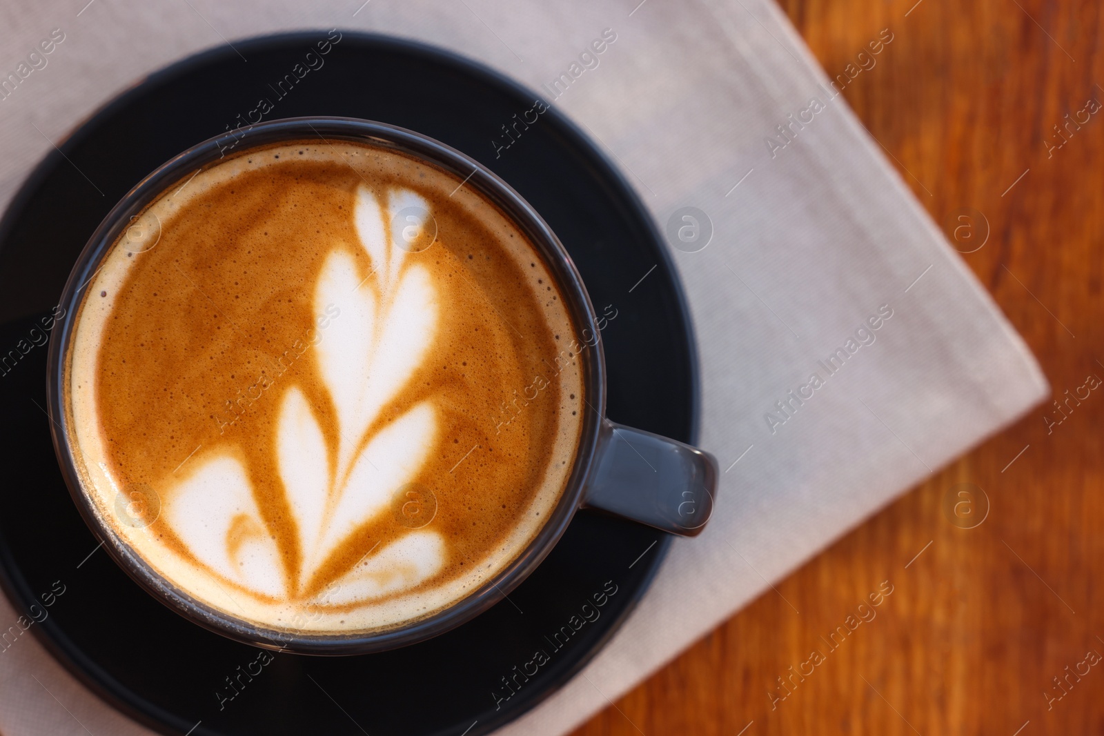 Photo of Cup of aromatic coffee with foam on wooden table, top view. Space for text