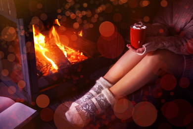 Woman with cup of delicious cocoa resting near fireplace at home, closeup. Winter vacation
