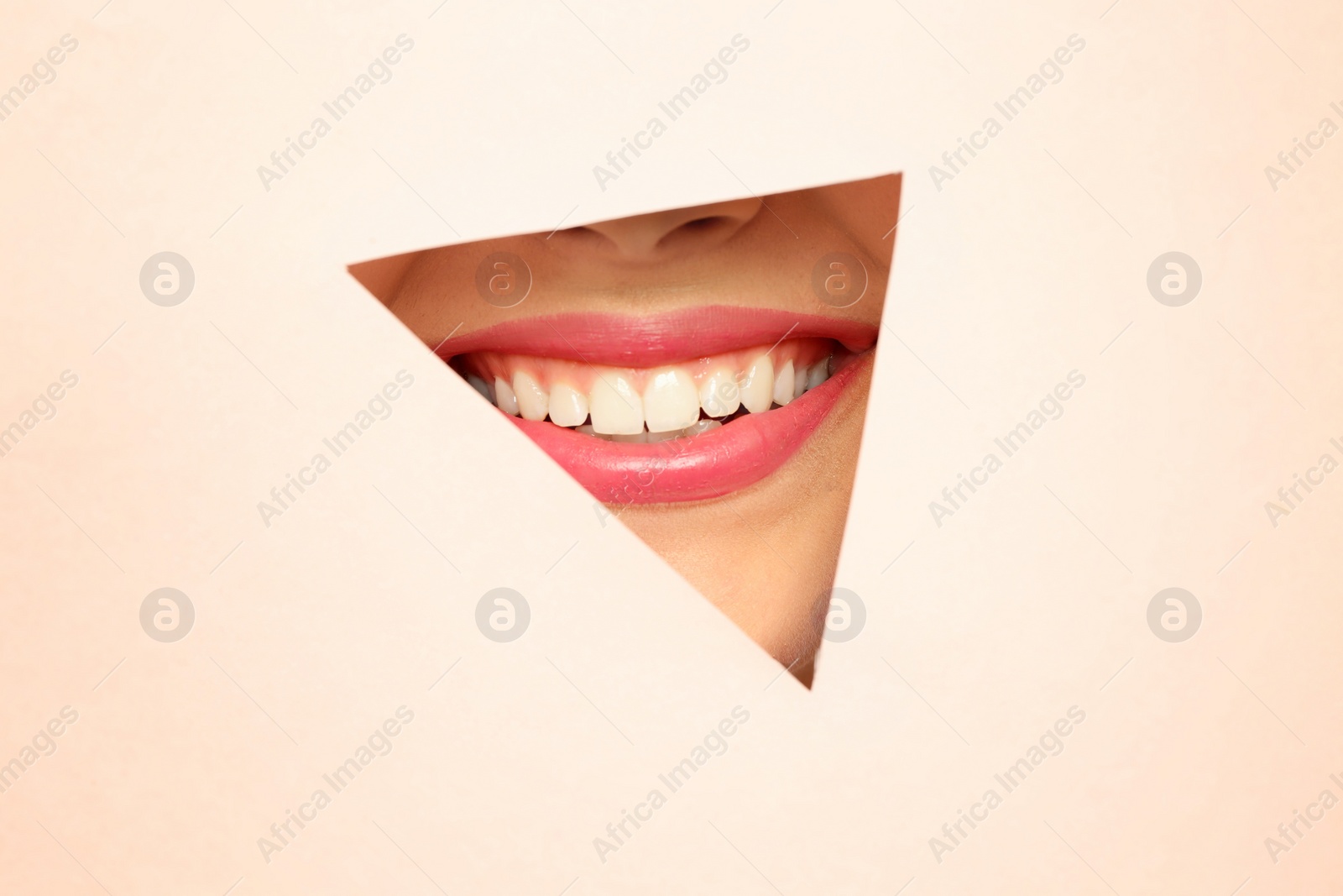 Photo of Young woman wearing beautiful lipstick, view through hole in color paper