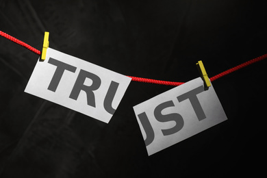 Photo of Cut word TRUST hanging on rope against black background. Concept of jealousy