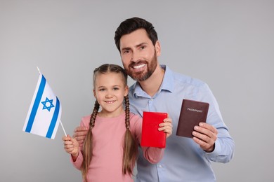 Immigration. Happy man with his daughter holding passports and flag of Israel on gray background