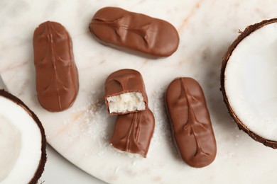 Delicious milk chocolate candy bars with coconut filling on white table, flat lay