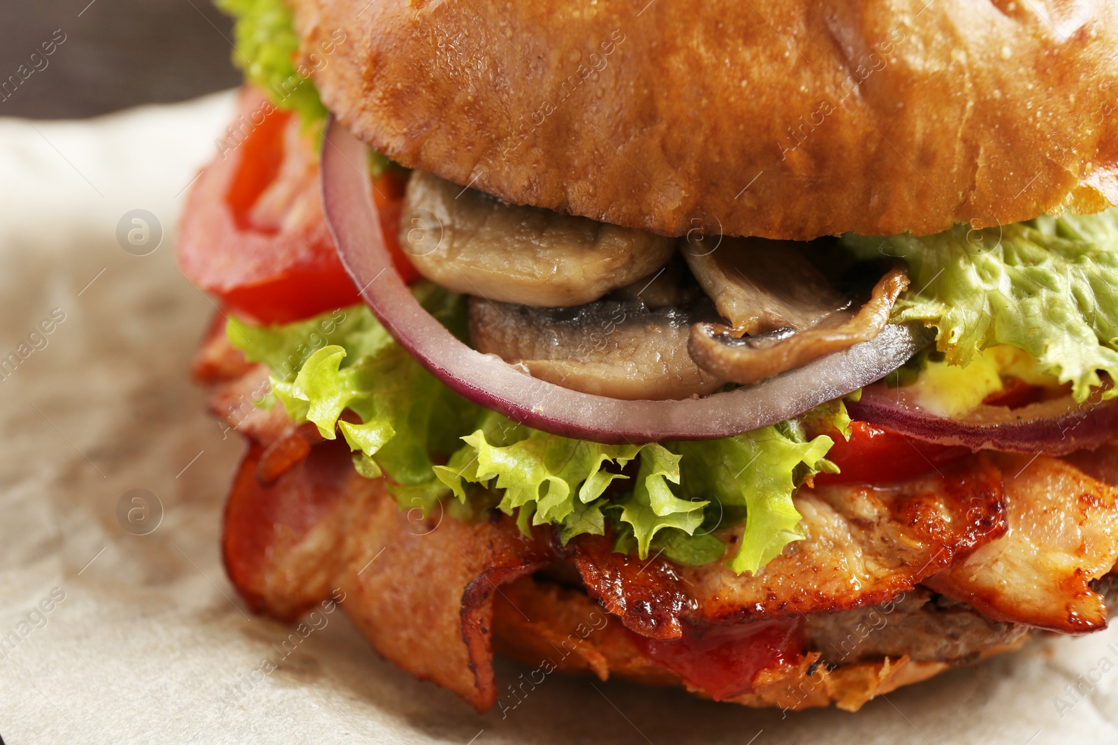 Photo of Delicious burger with bacon and mushrooms on parchment, closeup