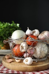 Photo of Fresh raw garlic and onions in metal basket on table against black background