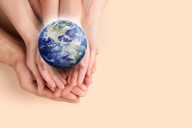 World in our hands. Top view of parents and kid holding digital model of Earth on beige background, space for text 