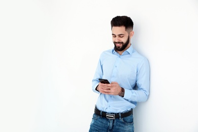 Photo of Handsome young man using phone near white wall, space for text. Working time