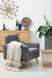 Photo of Stylish living room interior with comfortable armchair, blanket, side table and houseplant