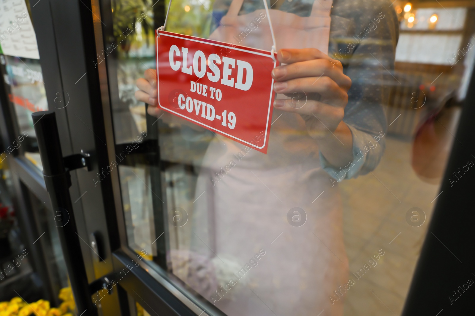 Photo of Woman putting red sign with words "Closed Due To Covid-19" onto glass door, closeup