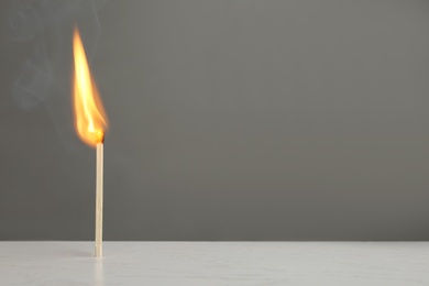 Photo of Lit match on table against grey background. Space for text