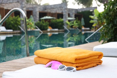 Beach towels and sunglasses on sun lounger near outdoor swimming pool. Luxury resort