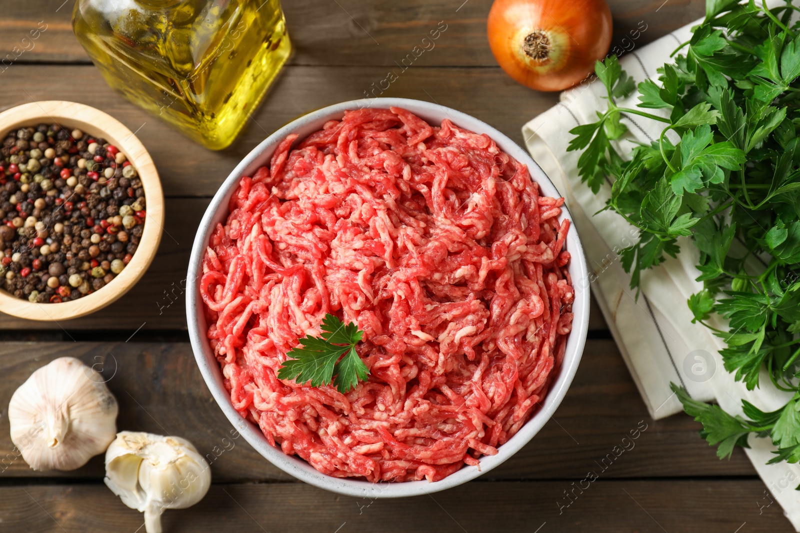 Photo of Raw ground meat in bowl, spices, oil and parsley on wooden table, flat lay