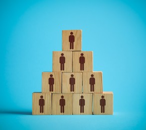 Team and management concept. Pyramid of wooden cubes with human icons on light blue background