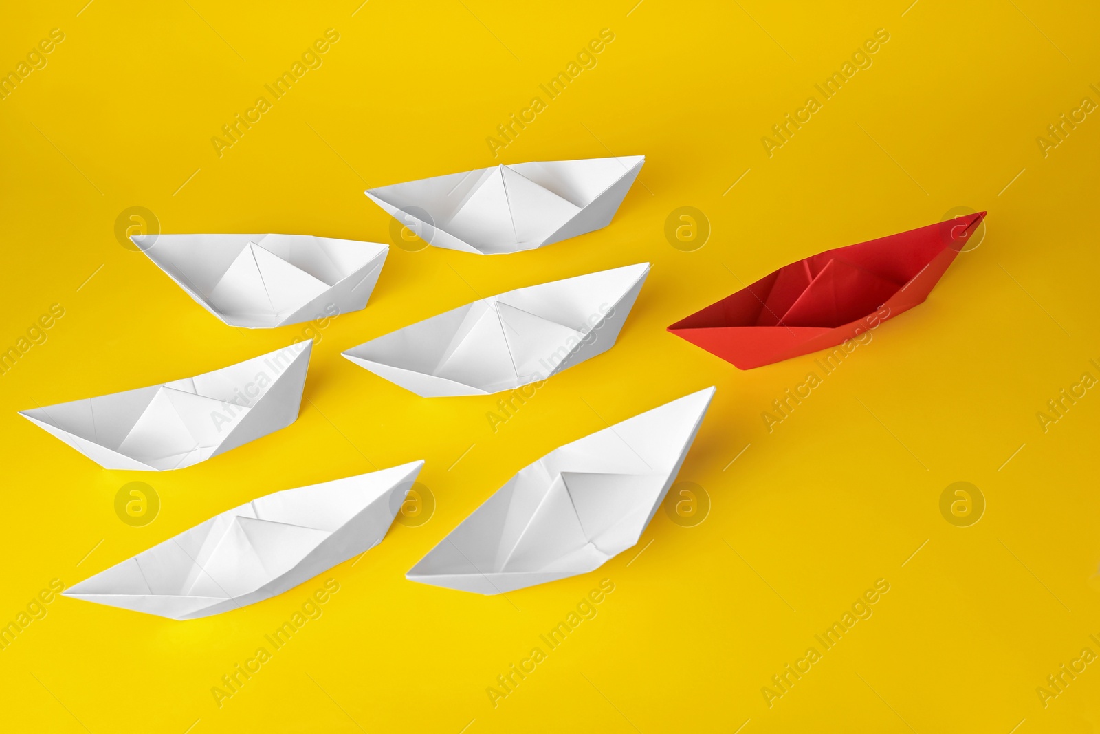 Photo of Group of paper boats following red one on yellow background. Leadership concept