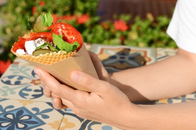 Photo of Woman holding wafer with falafel and vegetables at colorful tiled table outdoors, closeup. Street food