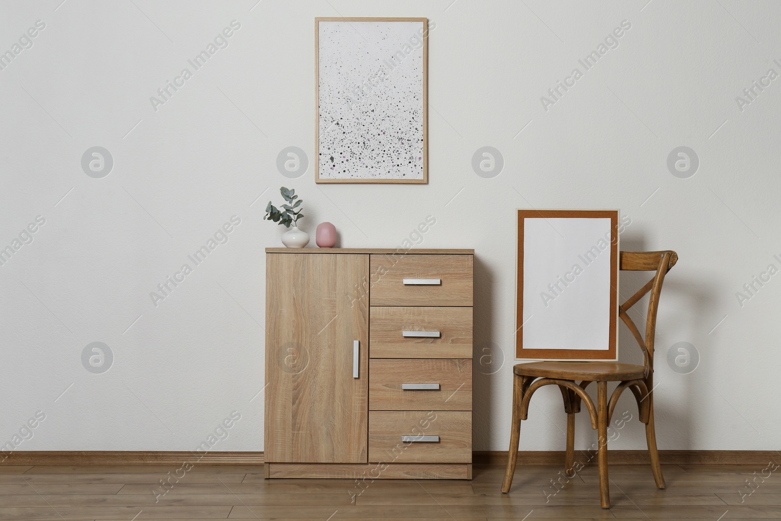 Photo of Wooden chair, chest of drawers, vases and frames in room with light wall. Interior design