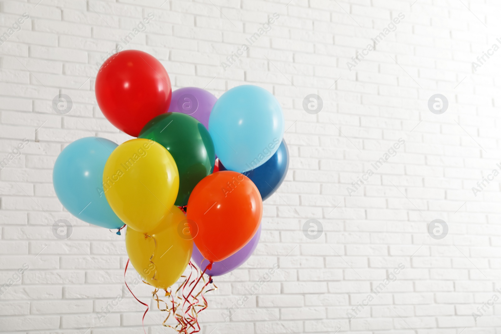 Photo of Bunch of bright balloons near brick wall, space for text. Celebration time