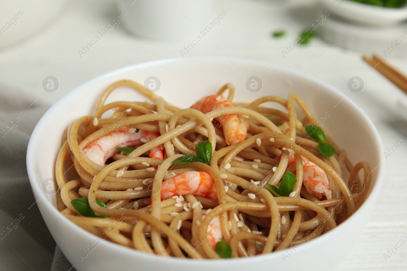 Photo of Tasty buckwheat noodles with shrimps in bowl on white wooden table, closeup