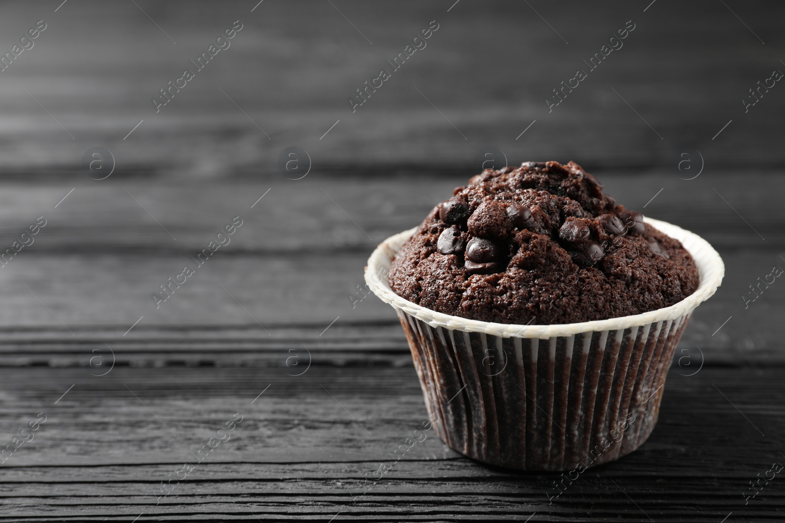 Photo of Delicious chocolate muffin on black wooden table, closeup. Space for text