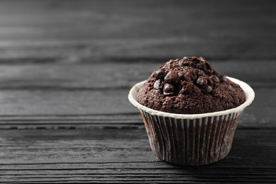 Photo of Delicious chocolate muffin on black wooden table, closeup. Space for text
