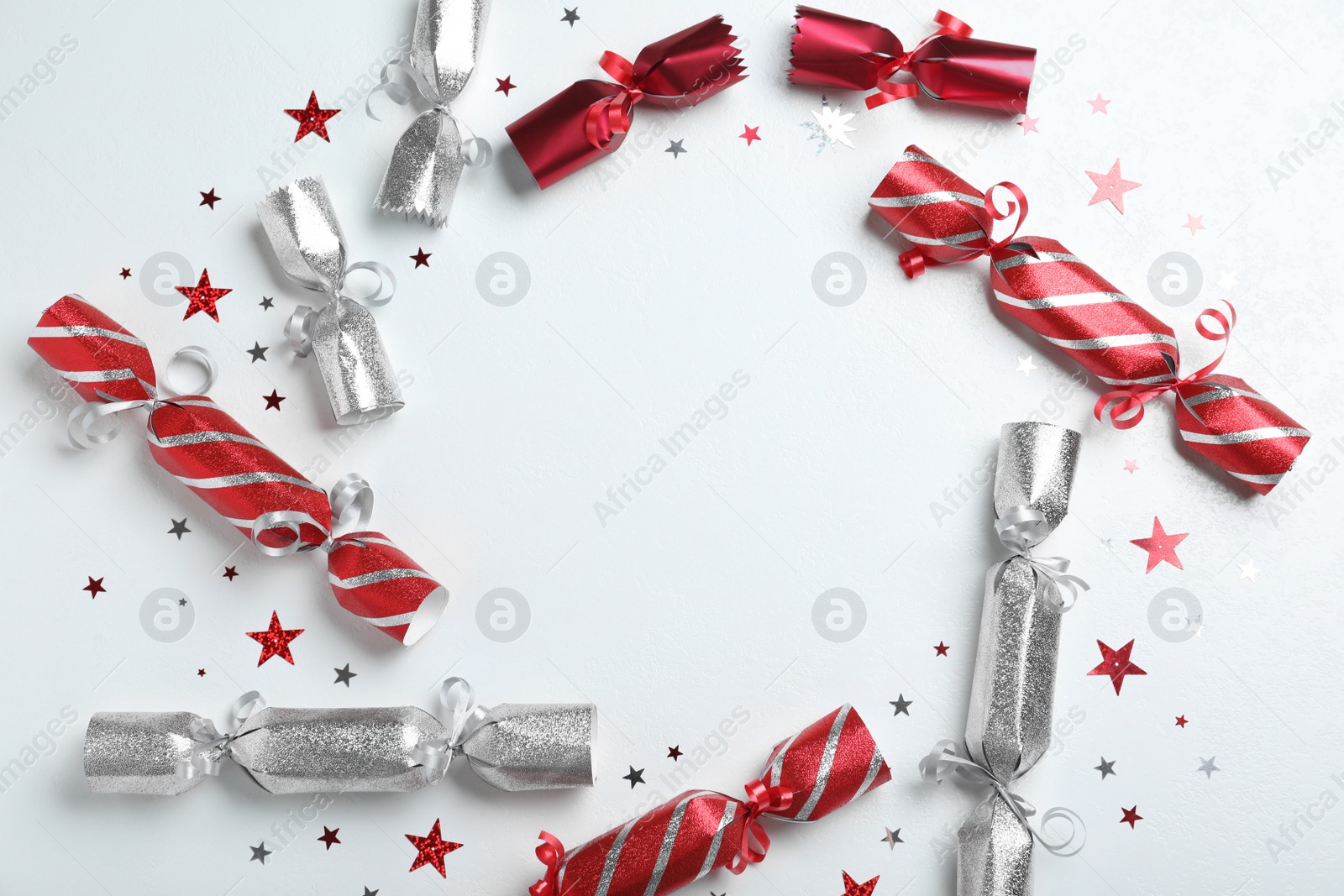Photo of Frame of Christmas crackers and shiny confetti on white background, flat lay. Space for text