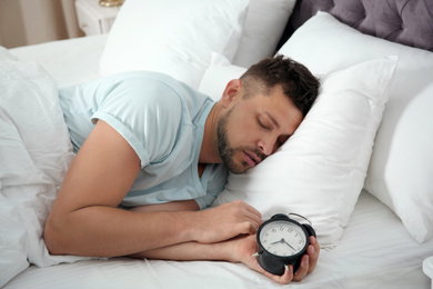 Man sleeping with alarm clock at home in morning