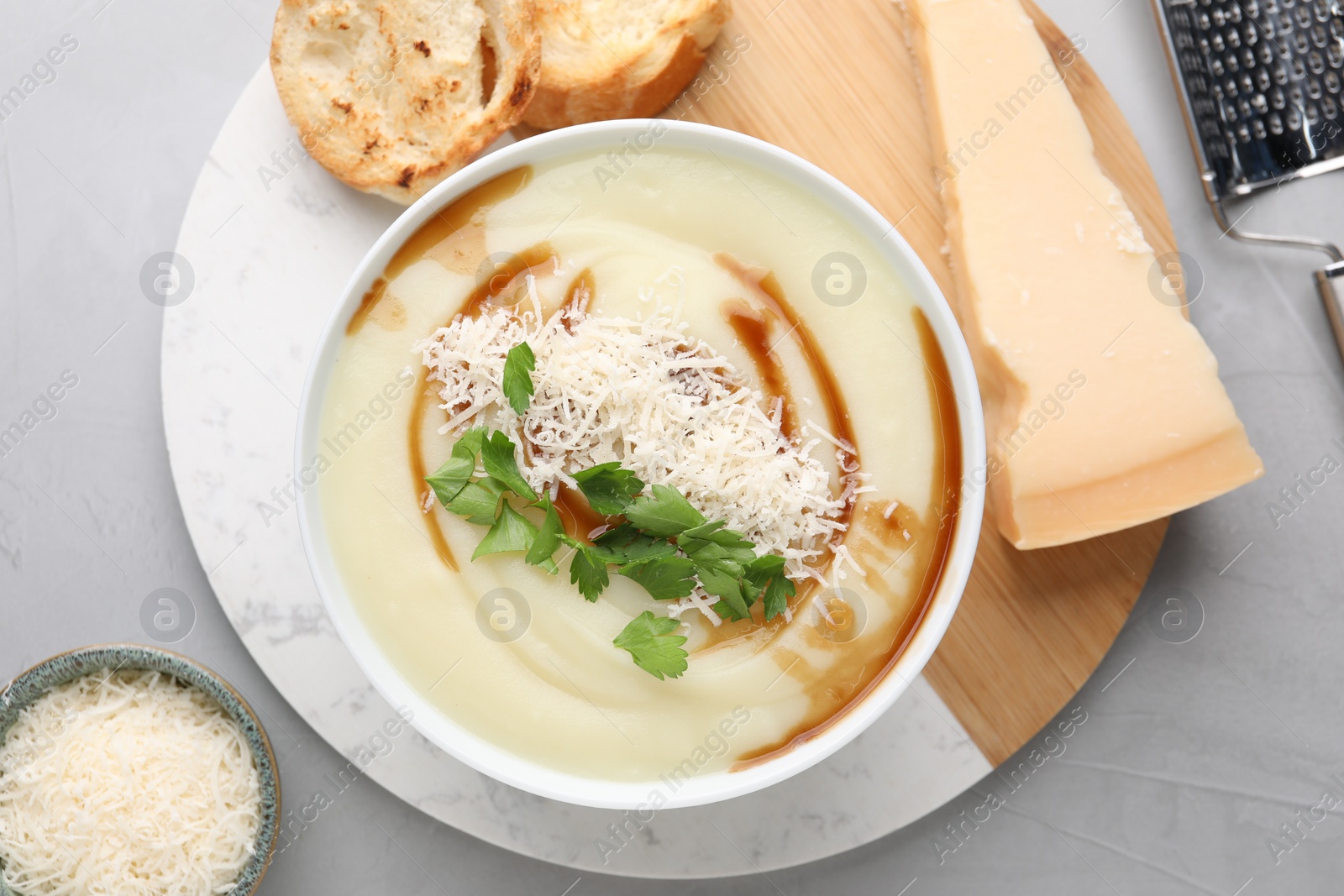 Photo of Delicious cream soup with parmesan cheese, soy sauce in bowl and croutons on light grey table, flat lay