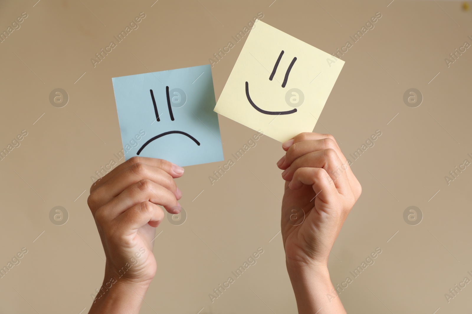 Photo of Choice concept. Woman holding papers with sad and happy emoticons on beige background, closeup