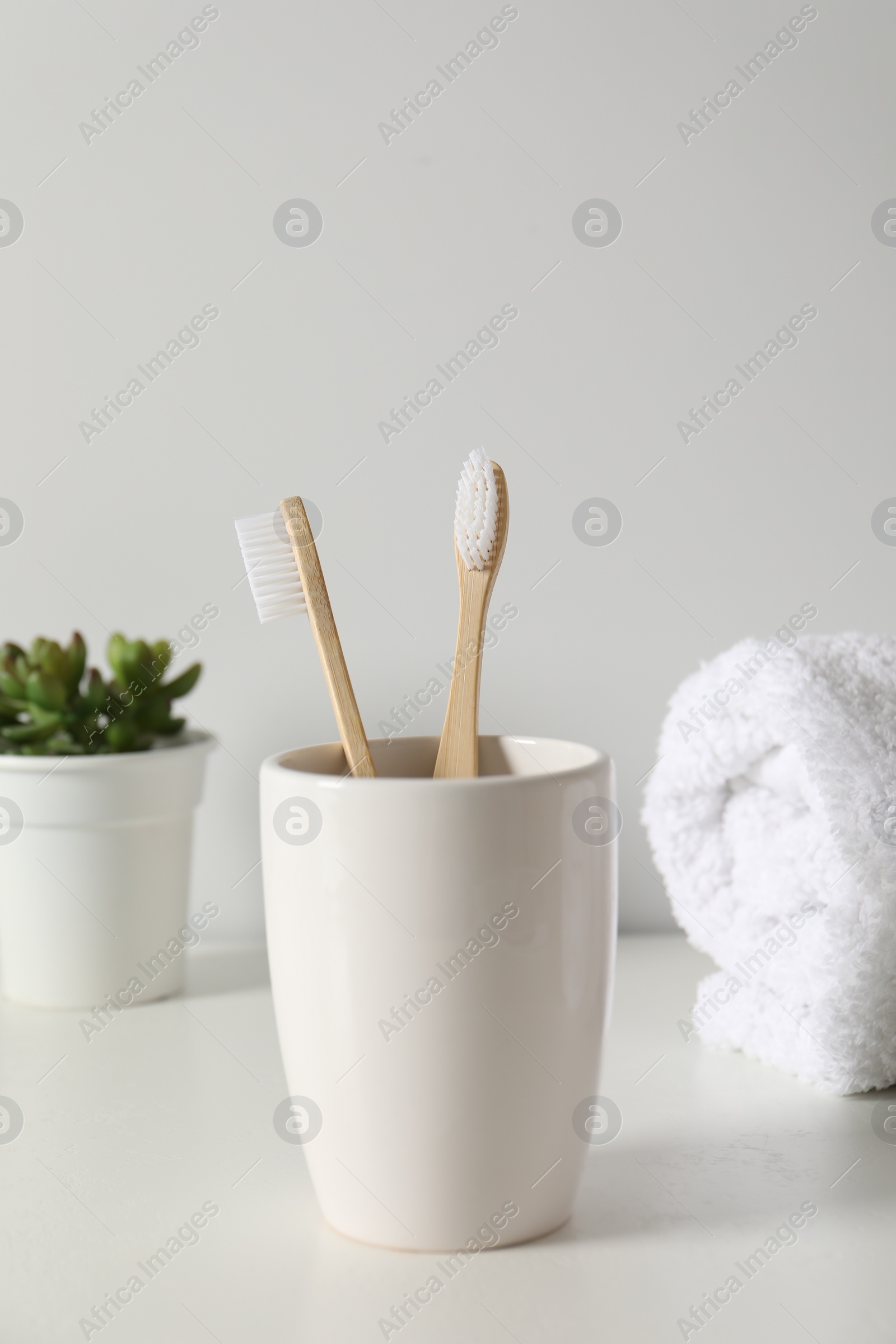 Photo of Bamboo toothbrushes in holder, potted plant and towel on white countertop